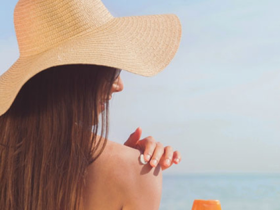 woman wearing straw hat, applying sunscreen to shoulder