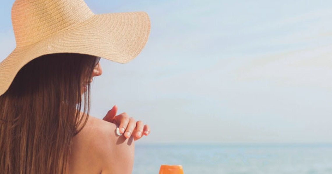 woman wearing straw hat, applying sunscreen to shoulder