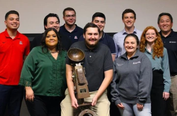 group of people standing, smiling, person in center holding trophy