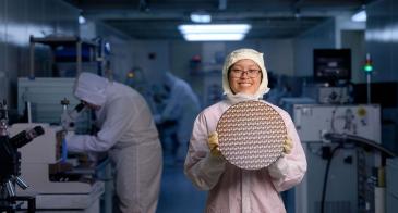 An engineering student wearing lab gear holds up a mechanical polish test wafer in a lab at the University of Arizona.